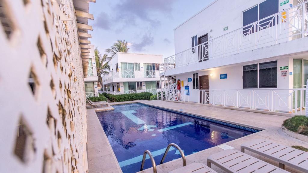 Piscina rectangular con agua azul, sillas blancas y entorno tropical en un complejo hotelero