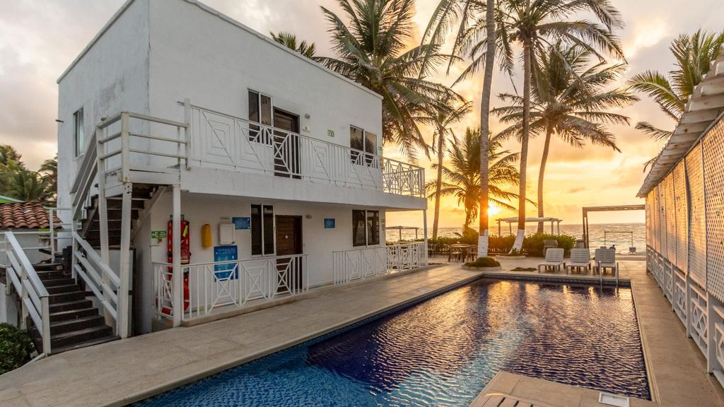 Piscina junto al atardecer sobre el océano, palmeras y zona de descanso