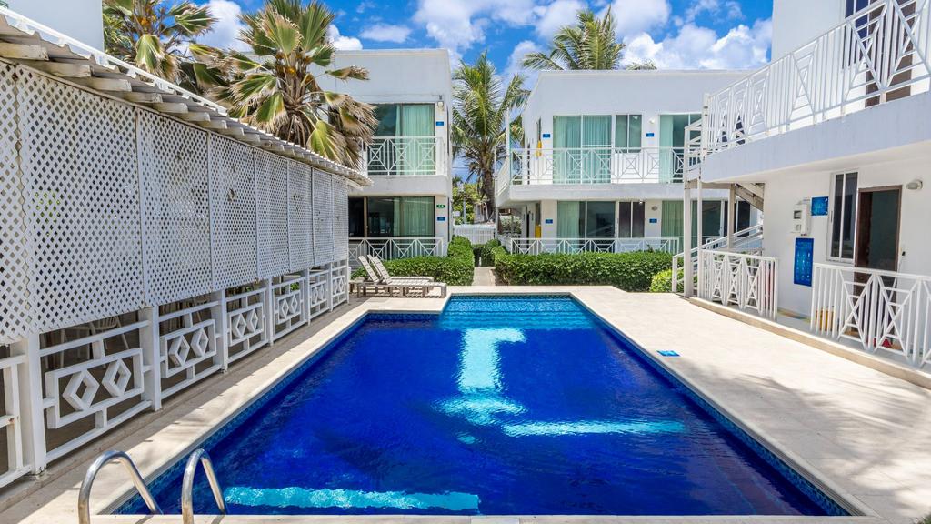 Piscina rodeada de edificios blancos, palmeras y sillas reclinables en un día soleado