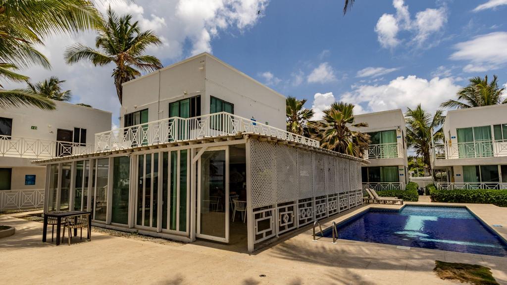 Piscina frente a edificio moderno blanco con balcones de vidrio, rodeado de palmeras