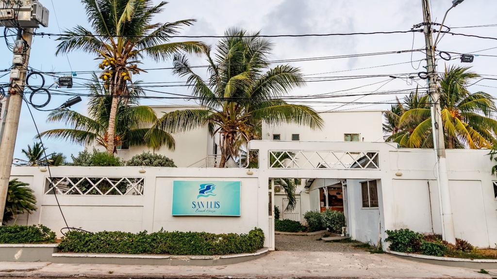 Vista exterior de San Luis Beach House con entrada enrejada, palmeras y entorno tropical.
