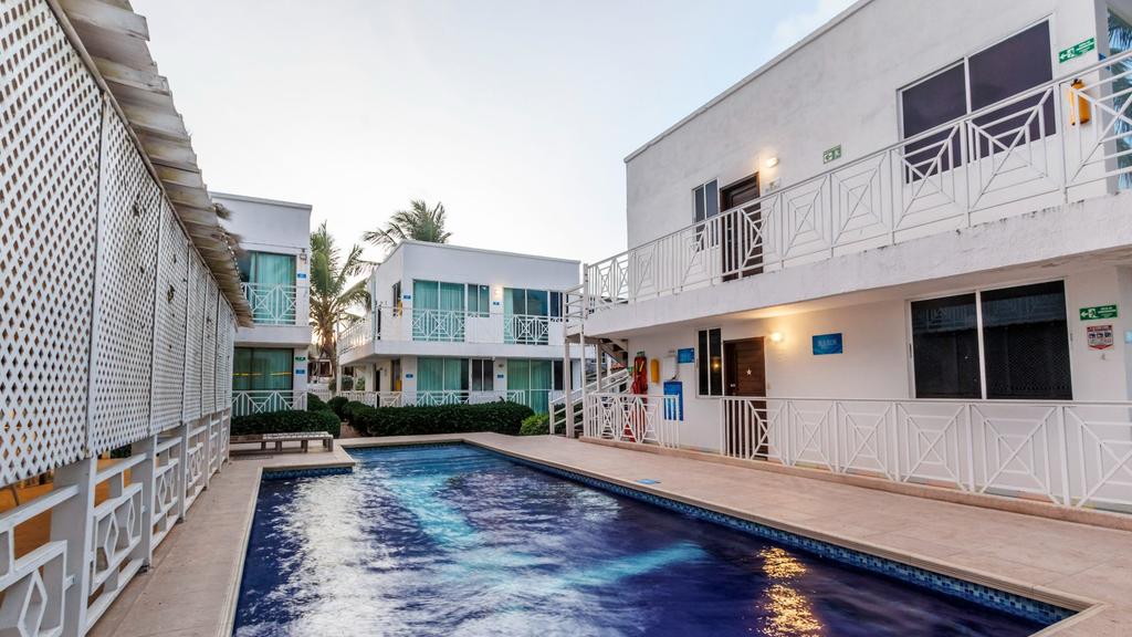 Piscina 3 frente a edificio moderno blanco con balcones de vidrio, rodeado de palmeras